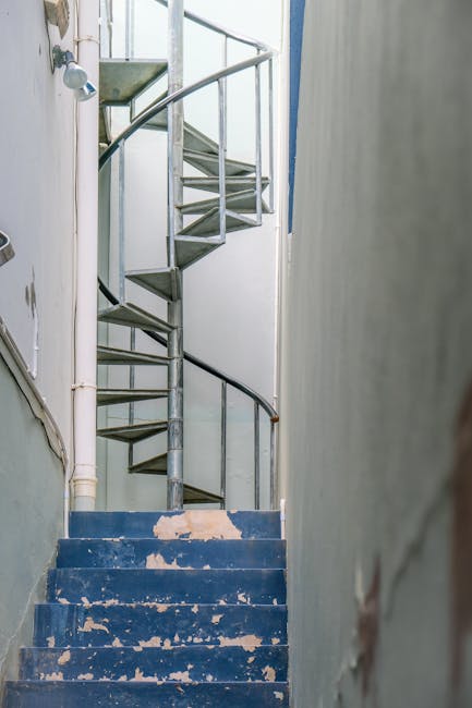 Close-up of a small interior staircase inside a property with two grey steps, each marked with yellow and black hazard tape along the edges. The staircase is framed by white walls and leads upward, wi