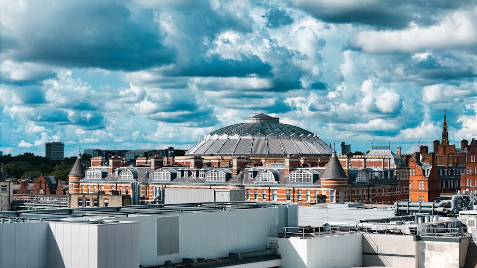 Photograph of the Royal Albert Hall in South Kensington, London, taken during daytime with natural lighting. The historic, circular building features a prominent domed roof and a detailed brick facade